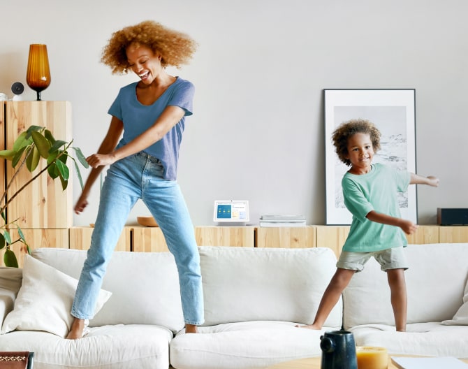 Google Nest Hub 2nd Gen on a shelf while a mother and son dance on their couch Google Nest Hub 2nd Gen on a shelf while a mother and son dance on their couch