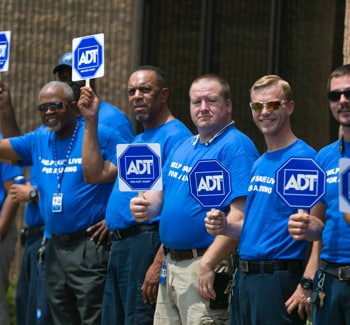 Group of people wearing blue shirts and holding ADT signs Group of people wearing blue shirts and holding ADT signs