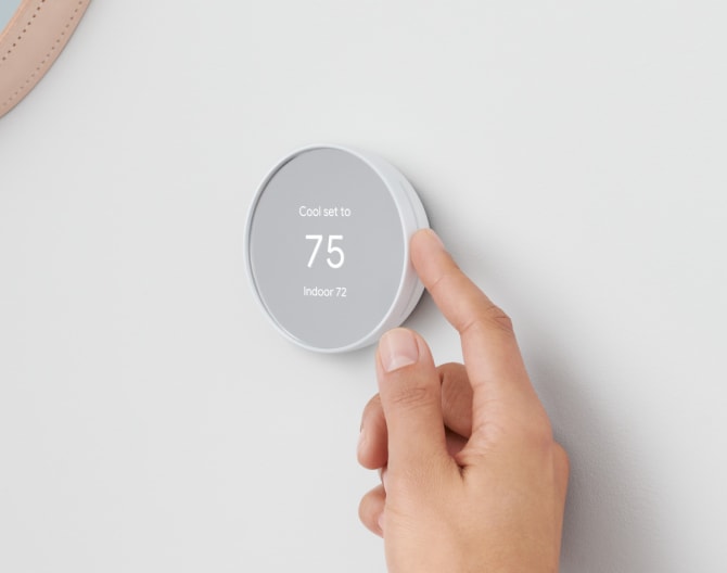 Google Nest Thermostat on a wall with a hand adjusting the temperature Google Nest Thermostat on a wall with a hand adjusting the temperature