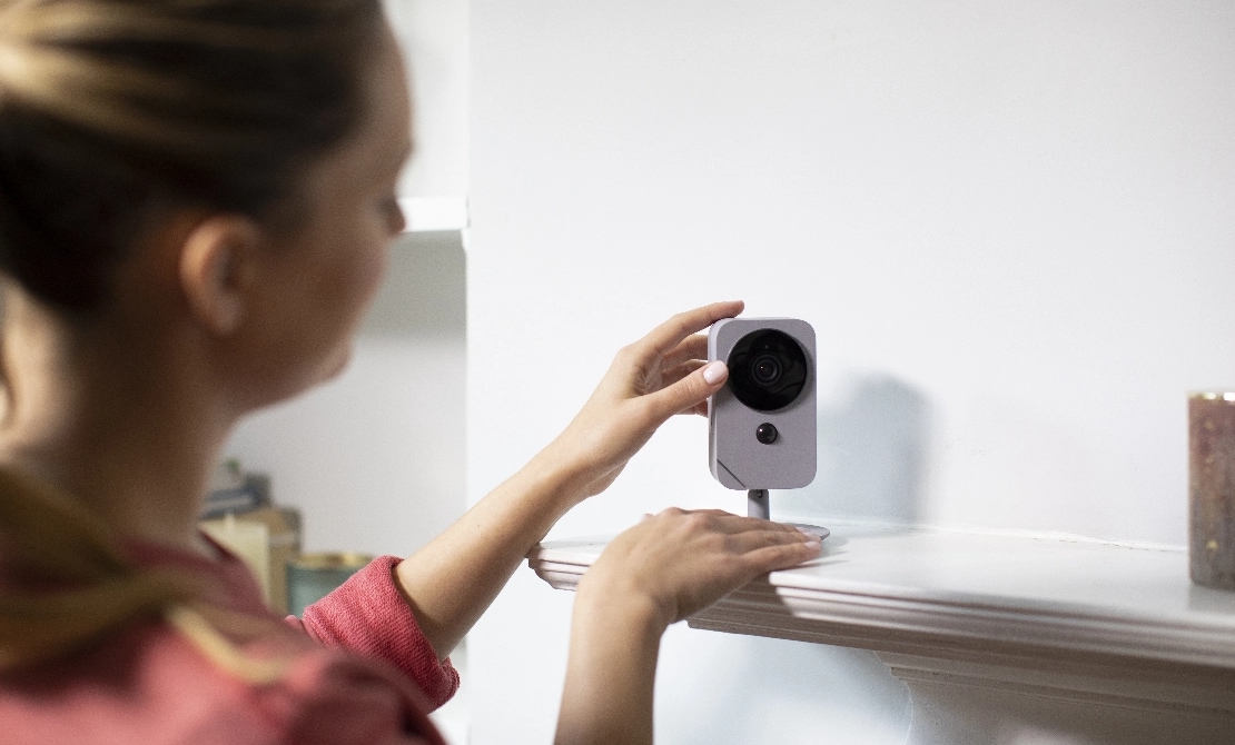 Woman self installing an ADT indoor camera on a shelf in her home Woman self installing an ADT indoor camera on a shelf in her home