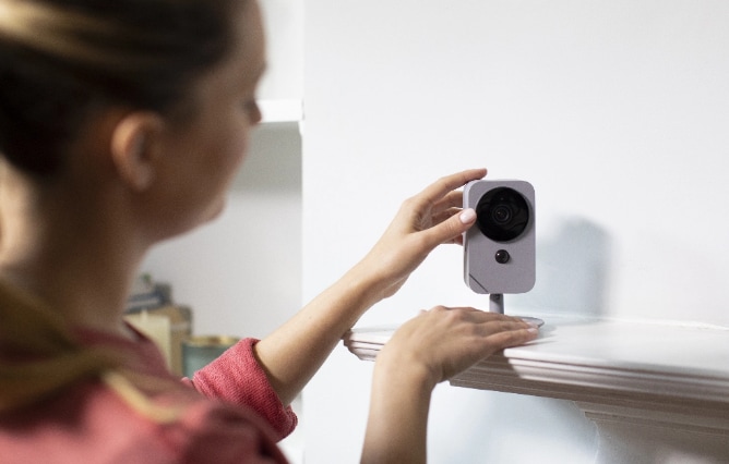 Woman self installing an ADT indoor camera on a shelf in her home Woman self installing an ADT indoor camera on a shelf in her home